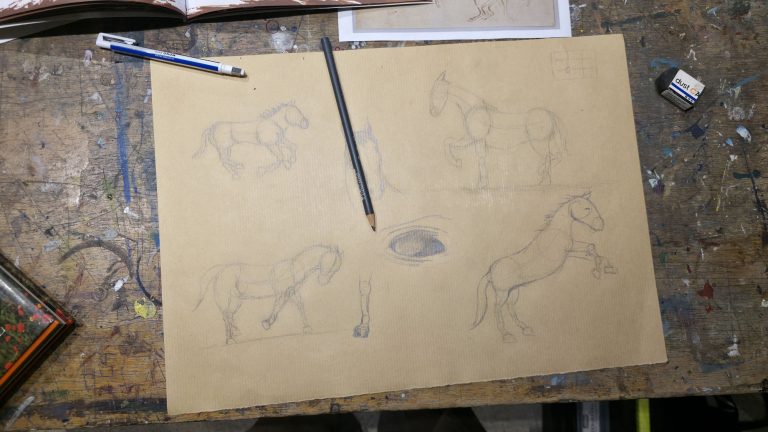 Photographie vue de haut d'une feuille de papier kraft avec plusieurs croquis au crayon de chevaux en mouvement, posée sur une table d'atelier tachetée de peinture.